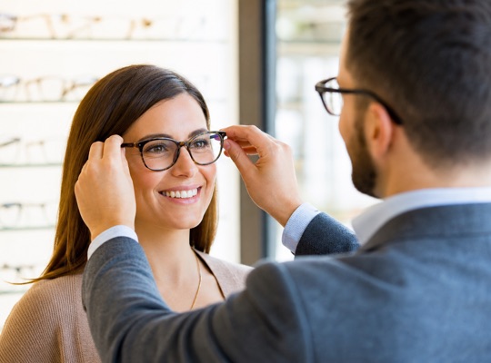 Optician adjusting a reading glasses frame on a smiling patient